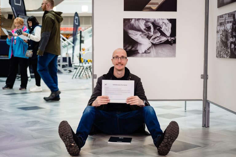 a man holding his award certificate sits on the floor in front of his award winning photo. It's rich of emma and rich photography.