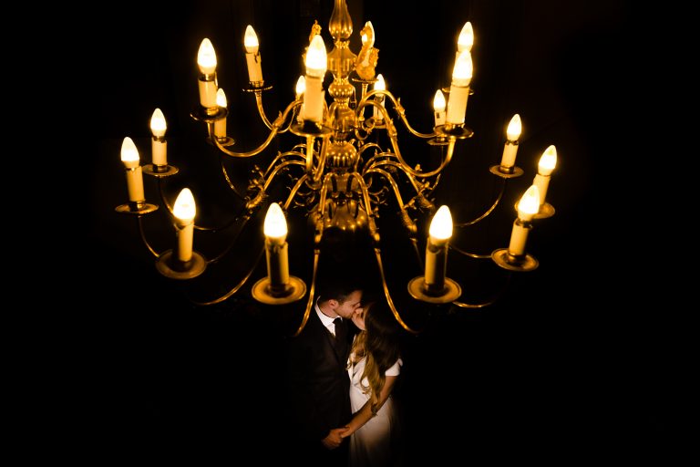 a bride and groom kiss beneath a chandelier. whitley hall wedding photography by emma and rich.