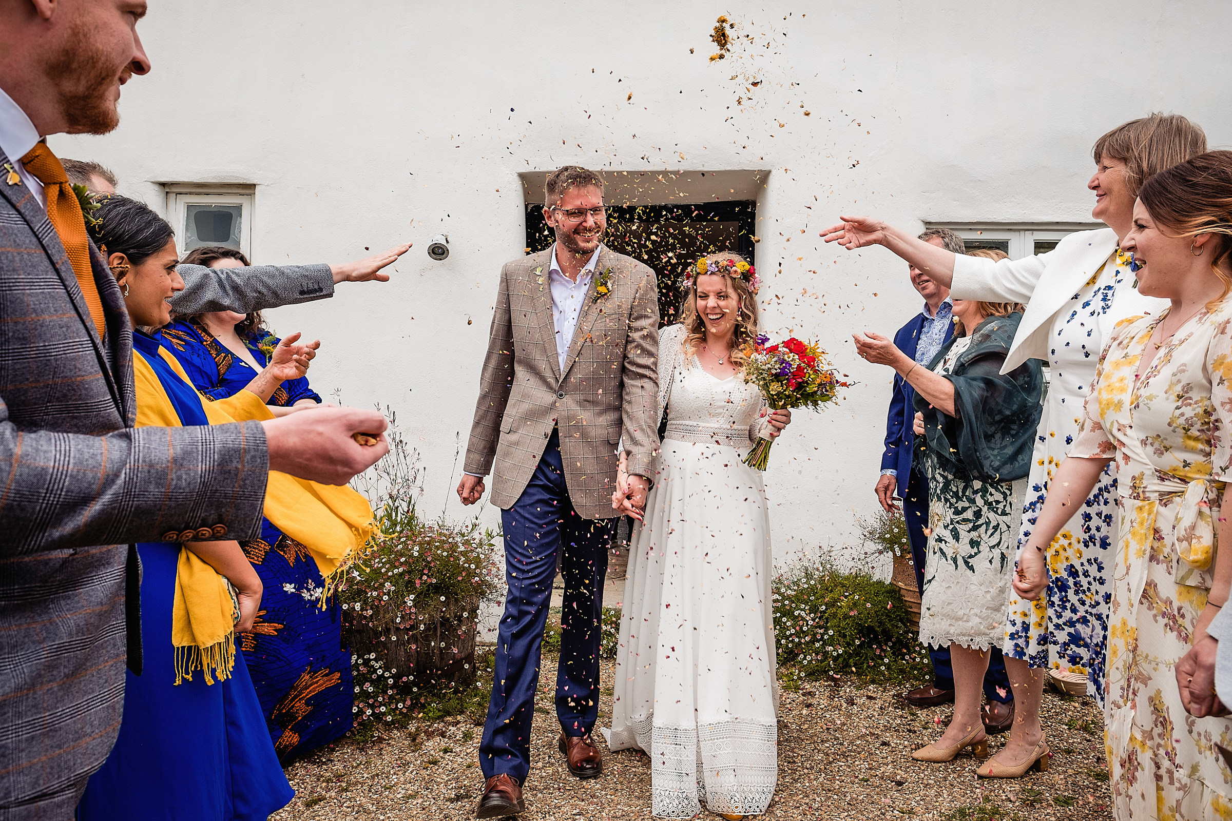 Bride and Groom walking through confetti outside the cottage at River Cottage. Fun wedding photography by Emma + Rich