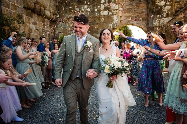 a bride and groom walking through a confetti shower. danby castle wedding photography by emma and rich.