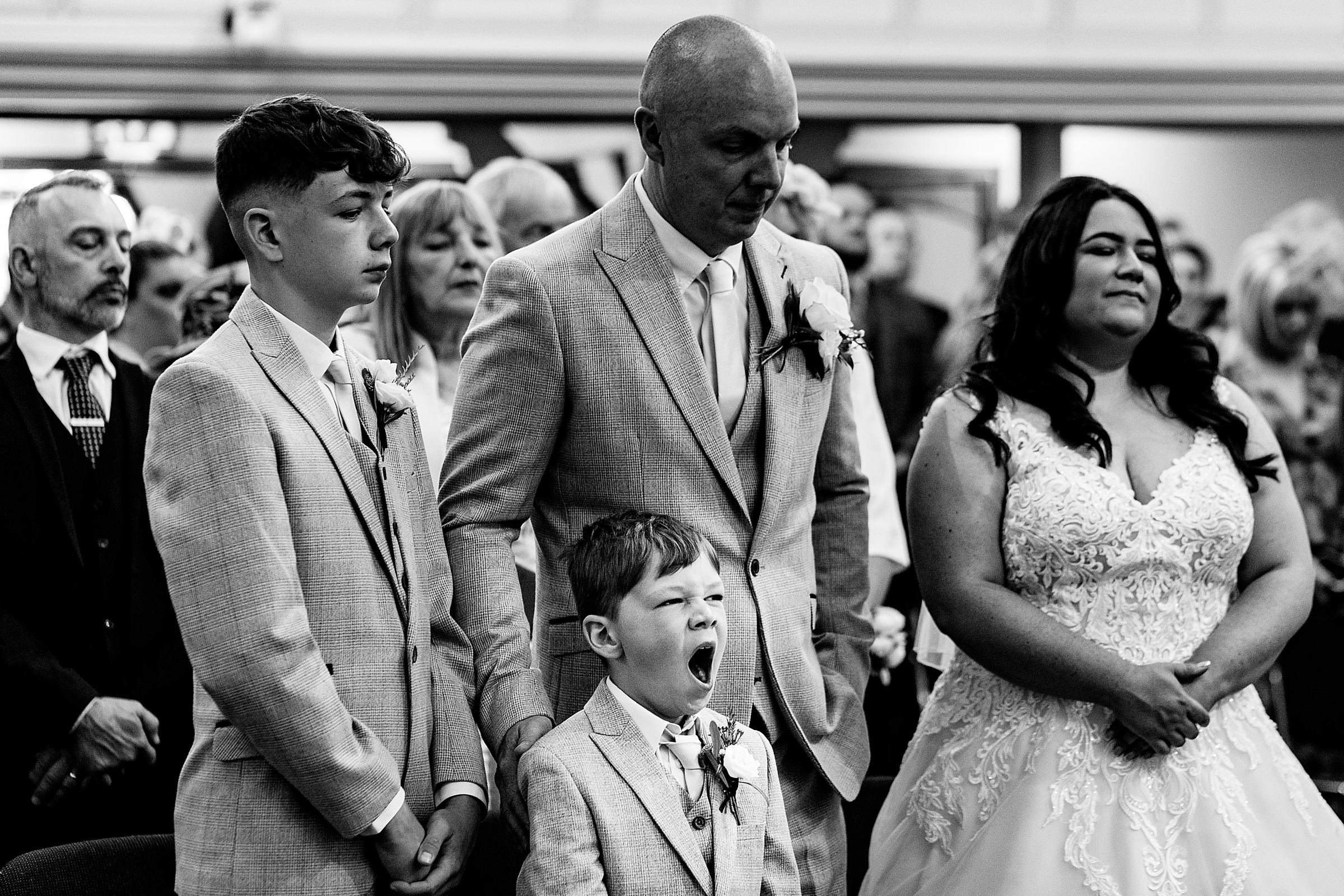 a young boy yawning at the front of a wedding ceremony. cheshire wedding photography by emma and rich.