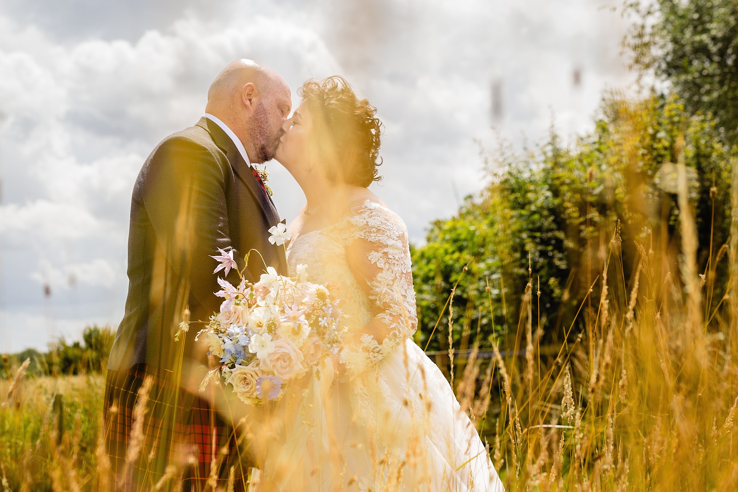 Newly married couple kissing in a wheat field. Abbey Farm Weddings wedding photography by Emma and Rich.